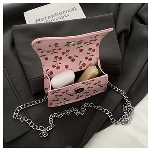 Close-up of a pink mini crossbody bag with cherry prints on a dark blazer and a book