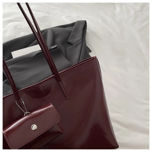 Close-up of glossy dark red tote bag with slim shoulder straps and matching mini pouch