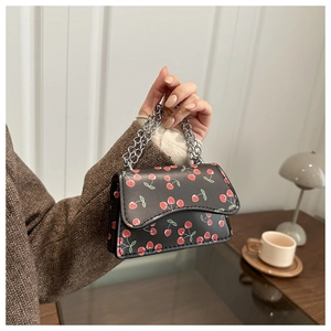 Detail of a black mini chain bag featuring vibrant red cherry prints and silver handles
