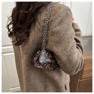 Detail of mini black flap bag with red cherry print and silver chain strap on model