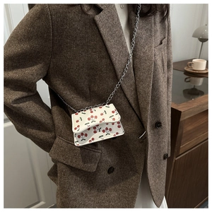 Close-up of a mini crossbody chain bag with red cherry prints on a white leather base