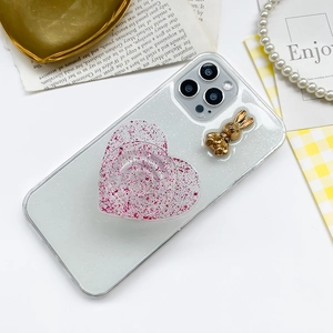 Detail of glitter heart phone grip and golden bunny charm on clear iPhone case