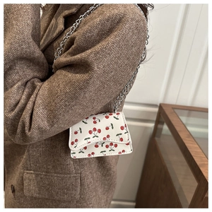 Close-up of a white mini crossbody bag with cherry prints and a silver chain strap