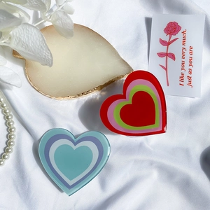 Detail of two-piece heart-shaped acrylic phone grips with color gradient on white fabric