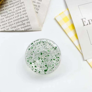 Close-up of circular phone grip featuring green glitter flakes and clear resin finish