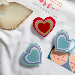 Flat lay of three layered colorful heart-shaped expanding phone grips on white fabric background