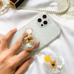 Close-up of a heart-shaped cartoon bear phone grip on a white lace phone case