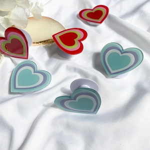 Collection of colorful heart-shaped acrylic phone grips arranged on white satin fabric