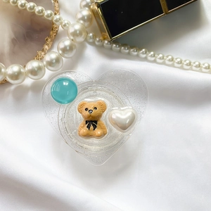 Close-up of heart-shaped phone grip with a brown bear and glitter elements on silk