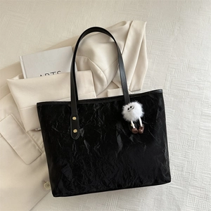 Black tote bag with pleated texture and white plush charm on a beige background