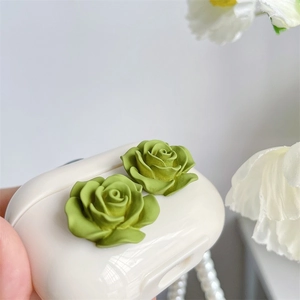 Detailed macro view of matte grass green camellia rose earrings on a white earphone case