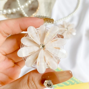 Macro detail of a 3D white flower phone grip with gold glitter and central diamond stud