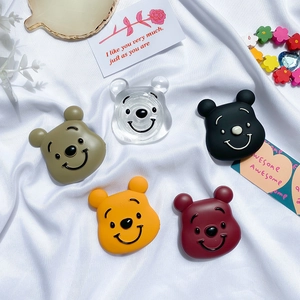 Cute bear-shaped expanding phone grip and stand in five colors on a white fabric background
