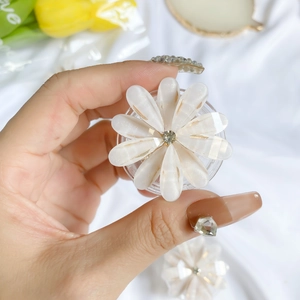 Close-up of white daisy phone griptok with central rhinestone held by hand on silk