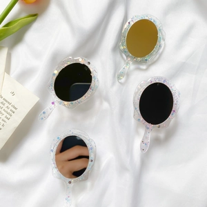 Close-up of portable oval makeup mirrors with glitter resin frames on silk fabric
