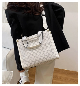Detail of a beige monogram tote bag featuring wide textile shoulder straps and metal rivets