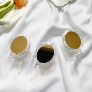 Three mini handheld acrylic mirrors with glitter details on white silk background