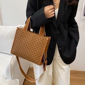 Brown monogram tote bag with wide strap and gold rivets in a minimalist studio setting