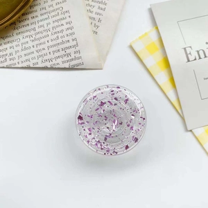 Round resin phone socket with purple glitter flakes and extendable grip on a white desk