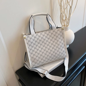 Fashionable monogram tote bag with wide strap displayed on a black cabinet