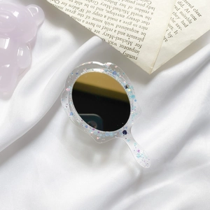 Close-up of portable hand mirror with blue glitter and resin frame on silk background