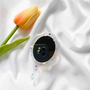 Close-up of wave-shaped portable mirror with colorful glitter on white silk fabric