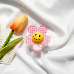 Detail of pink plaid flower phone grip with yellow smiley face on white silk fabric