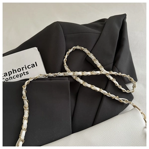 Close-up of white litchi leather bag with gold chain strap on black blazer background