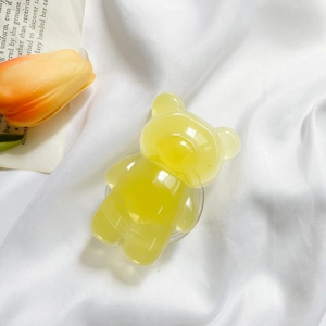 Macro shot of translucent yellow bear phone grip on a white silk fabric background