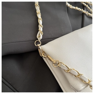 Detail of white lychee leather texture and golden metal chain strap on a crossbody bag