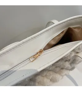 Detailed close-up of smooth gold metal zipper hardware on a plush cream bucket bag