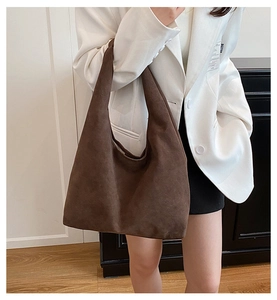 Close-up of a large brown suede tote bag styled with a white blazer and black pants