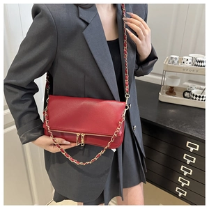 Red pebbled leather crossbody bag with gold chain strap shown on model over grey blazer