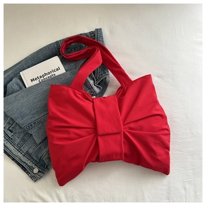 Flat lay of bright red bow-shaped handbag on white background with blue denim jacket