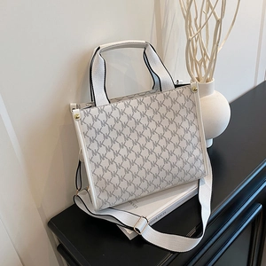Cream monogram tote bag with MK print and black woven strap on a dark display