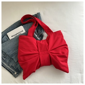 Flat lay view of a large red bow-shaped tote bag with wide shoulder straps on white fabric