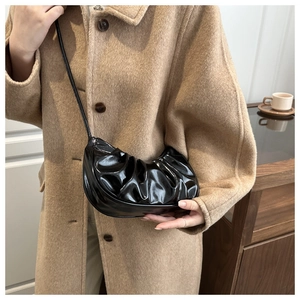 Dettaglio della borsa a pieghe nera lucida indossata da una modella con cappotto di lana