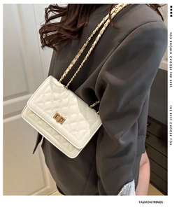 Detail of white quilted leather crossbody bag with gold chain strap on grey blazer