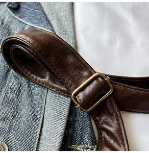 Détail macro de la bandoulière en cuir grainé marron foncé avec boucle dorée