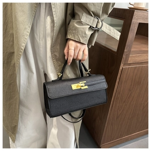 Detail of elegant black leather handbag with a signature golden twist lock on a beige coat