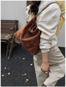 Brown suede tote bag with white quilted stitching and metal chain strap worn by a model