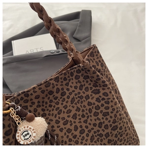 Detail of leopard print tote bag featuring a woven handle and a cupcake plush charm accessory