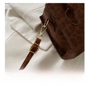 Close-up of golden metal hooks and leopard print texture on a suede crossbody bag
