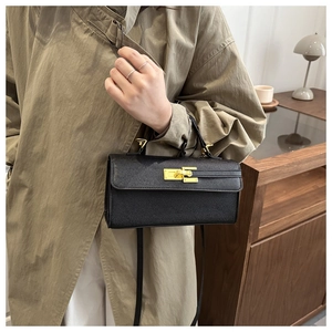 Detail of minimalist black textured leather bag featuring a gold metal twist lock and strap