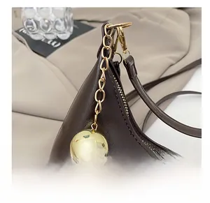 Detailopname van bruine leren tas met gouden bolhanger en stevige ritssluiting