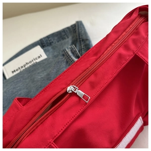 Close-up of top zipper closure on red nylon shoulder bag with twill fabric texture