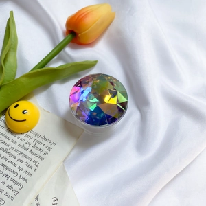 Close-up of iridescent faceted crystal phone socket grip on white satin fabric background