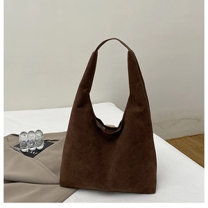 Detail of a large brown suede hobo tote bag placed on a white surface with props