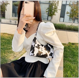 Detail of cow print baguette bag shown in a sunny park with stylish fashion outfit