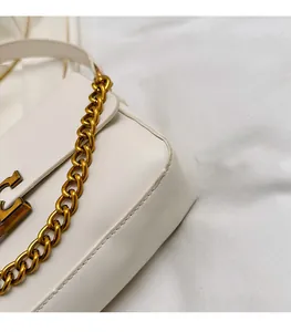 Macro shot of white leather crossbody bag with chunky gold chain and logo detailing